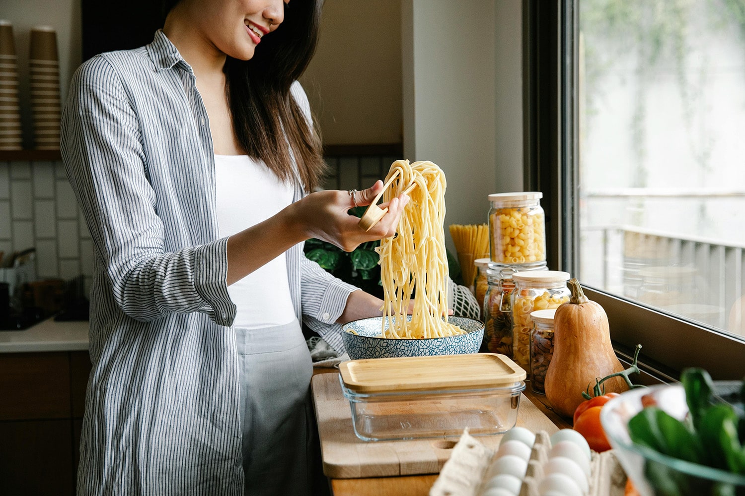 A woman is preparing a bowl of spaghetti while in the kitchen.
