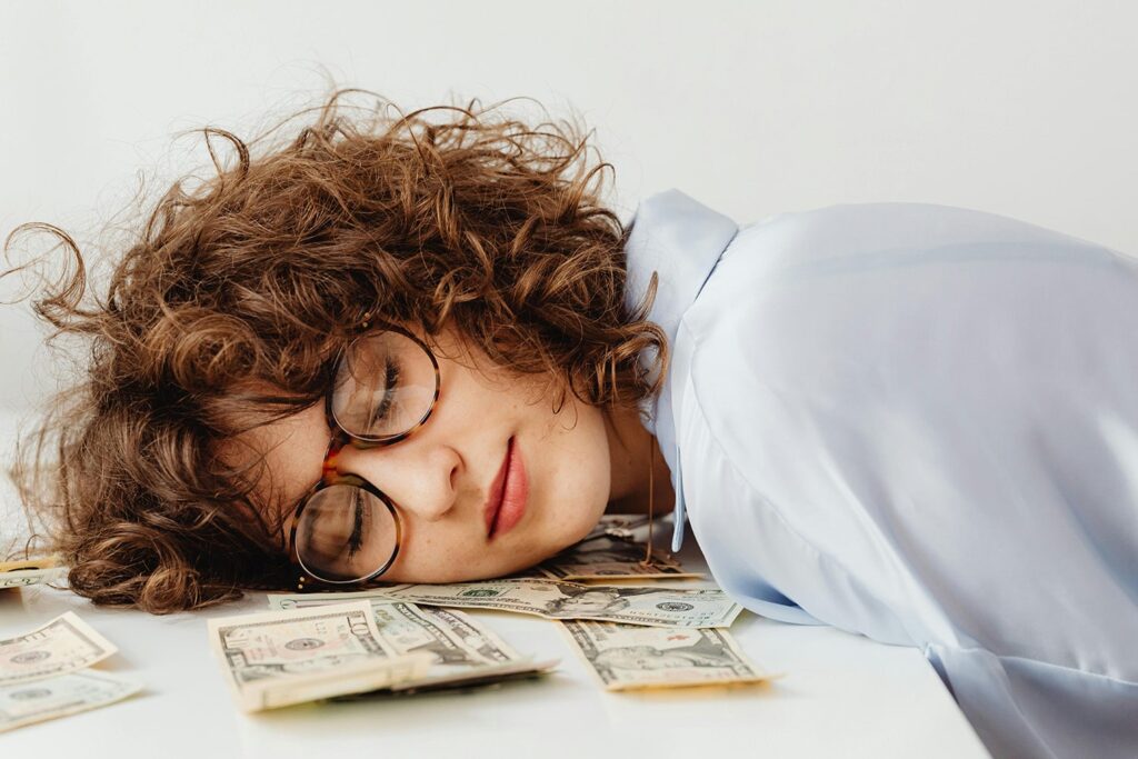 Woman with her eyes closed and head on the table, on top of money.